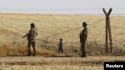 Turkish soldiers stand guard as a Syrian refugee boy waits behind the border fences to cross into Turkey on the Turkish-Syrian border, near the southeastern town of Akcakale in Sanliurfa province, Turkey, June 5, 2015.