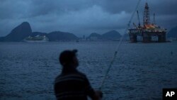 FILE - A man fishes in Guanabara Bay where an oil platform floats, backdropped by Sugar Loaf Mountain, left, in Niteroi, Brazil, April 21, 2015.