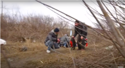 A YouTube screen capture from a March 6, 2022, BBC report, "Horrific scenes in battle for Kyiv as families killed fleeing Russian onslaught - BBC News," shows civilians taking shelter from Russian artillery shelling on a river embankment while attempting to flee Irpin.