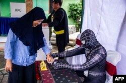 Seorang petugas KPPS dengan kostum superhero membantu seorang pemiih mendaftar di TPS di Surabaya, 17 April 2019.