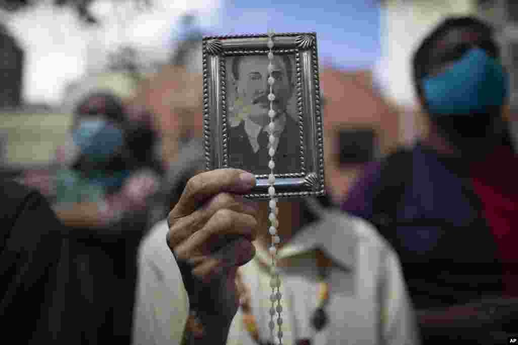 A devotee of late Venezuelan Dr. Jose Gregorio Hern&#225;ndez holds up his picture and a rosary outside La Candelaria church where he is buried in Caracas, Venezuela, Monday, Oct. 26, 2020. The remains of the doctor popularly known as the &quot;Saint of the Poor&quot; 
