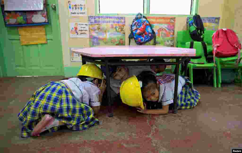 Para murid sekolah dasar berlindung di bawah meja di kelas mereka pada saat latihan menghadapi gempa bumi di Paranaque City, Metro Manila, Filipina.