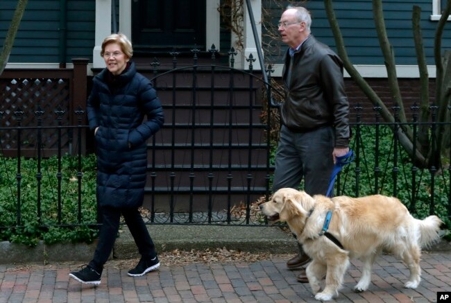 Democratic Sen. Elizabeth Warren steps outside her home with her husband Bruce Mann, right, and their retriever Bailey, Dec. 31, 2018, in Cambridge, Massachusetts, where she confirmed that she is launching an exploratory committee to run for president.