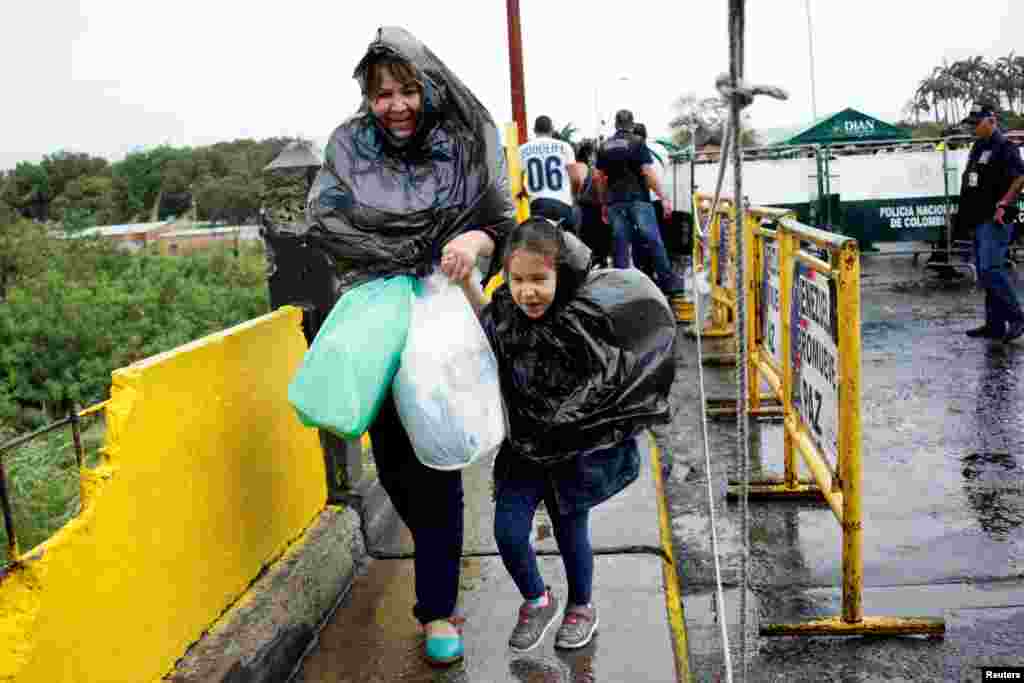 A woman and a child use plastic bags to cover from the rain as they cross the Colombian-Venezuelan border over the Simon Bolivar international bridge after shopping, in San Antonio del Tachira, Venezuela, July 16, 2016.