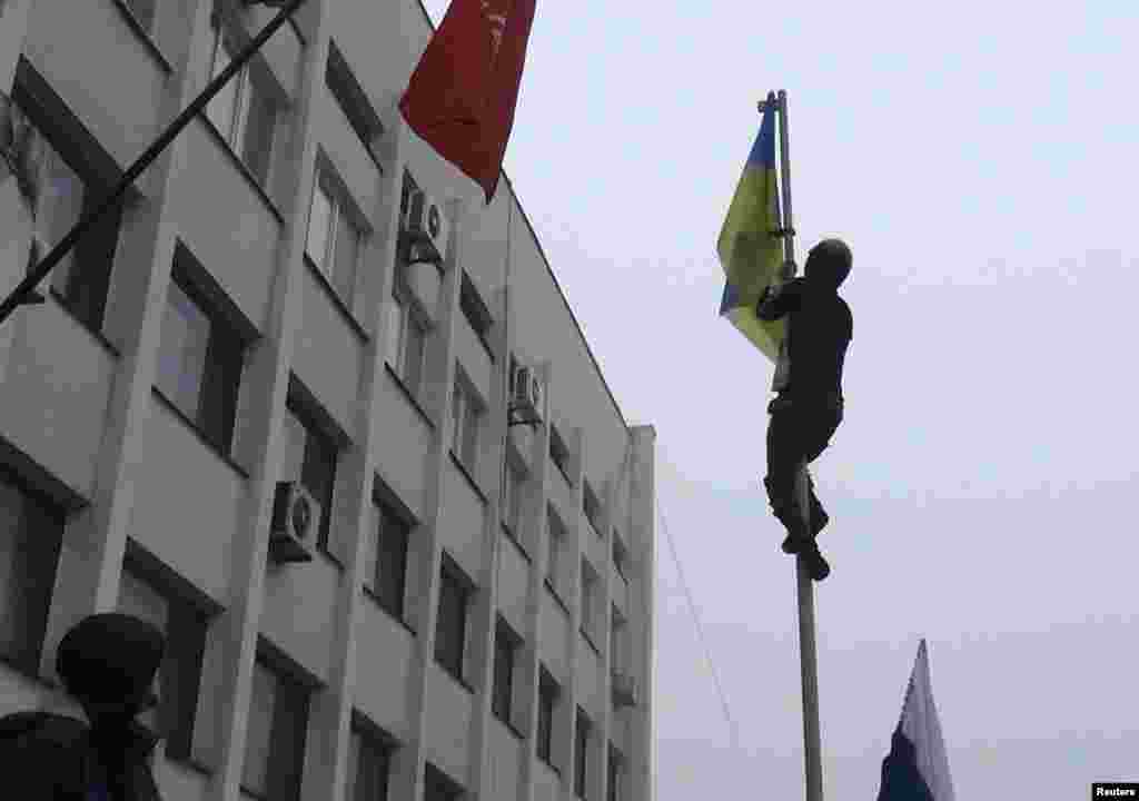 Seorang pria memanjat tiang untuk mencopot bendera Ukraina di tengah demonstrasi di luar kantor walikota Mariupol, Ukraina timur (13/4).