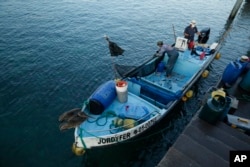 In this May 2, 2020 photo, fishermen work in their boat in the bay of San Cristobal, Galapagos Islands, Ecuador. Locals like to joke that, "In the Galapagos, it is prohibited to get sick." But COVID-19 has upended any sense of island immunity.