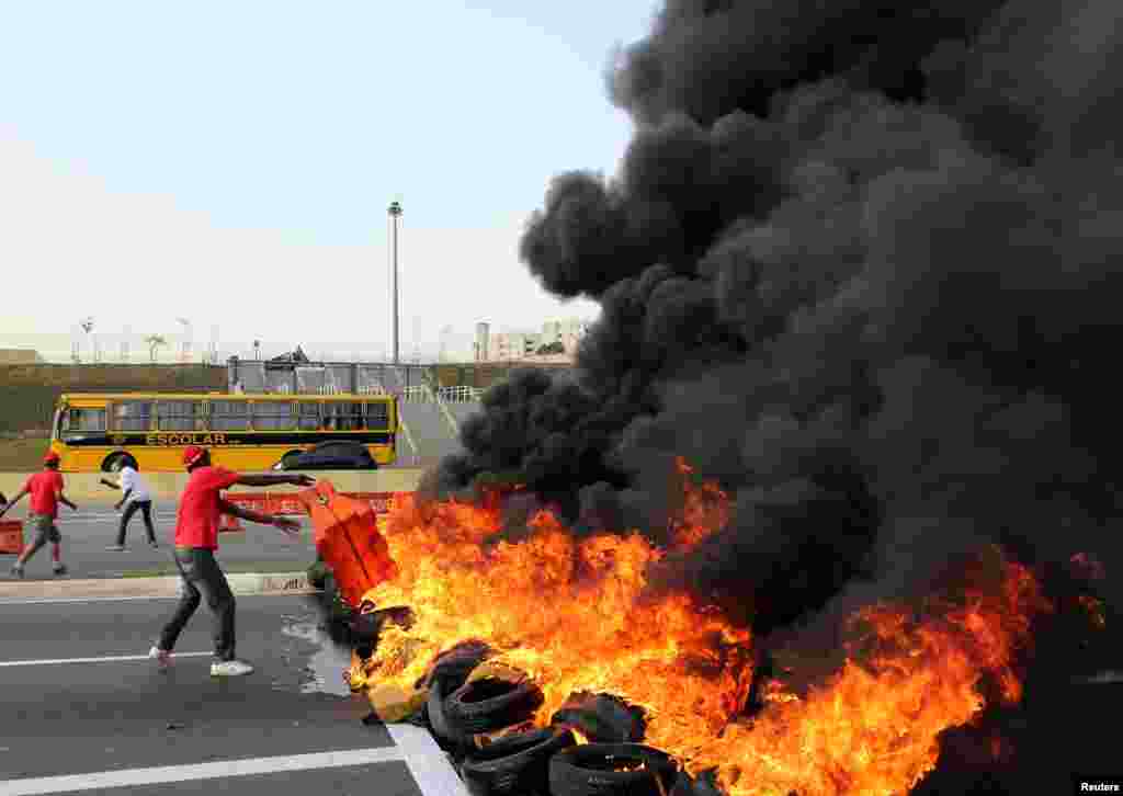 A supporter of Brazil's suspended President Dilma Rousseff throws a traffic barrier to make a burning barricade to block a main avenue next to Arena Sao Paulo stadium, in Sao Paulo, Brazil.