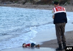 A Turkish police officer stands next to a migrant child's dead body (Aylan Kurdi) off the shores in Bodrum, southern Turkey, on Sept. 2, 2015 after a boat carrying refugees sank while reaching the Greek island of Kos.
