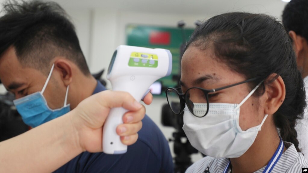 A local journalist, right, has her temperature checked to cover a handover ceremony of a donation in Phnom Penh, Cambodia, Saturday, March 28, 2020. Cambodia held the ceremony to receive a donation from Alibaba and Jack Ma foundation of its 20,000 COVID-19 test kits prevention.