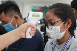 A local journalist, right, has her temperature checked to cover a handover ceremony of a donation in Phnom Penh, Cambodia, Saturday, March 28, 2020. Cambodia on Saturday held the ceremony to receive a donation from Alibaba and Jack Ma foundation of its 20,000 COVID-19 test kits for prevention, control and response to the new coronavirus in Cambodia. (AP Photo/Heng Sinith)