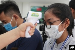 FILE - A local journalist, right, has her temperature checked to cover a handover ceremony of a donation in Phnom Penh, Cambodia, Saturday, March 28, 2020. Cambodia on Saturday held the ceremony to receive a donation from Alibaba and Jack Ma foundation of its 20,000 COVID-19 test kits for prevention, control and response to the new coronavirus in Cambodia. (AP Photo/Heng Sinith)