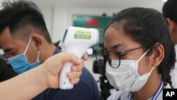 A local journalist, right, has her temperature checked to cover a handover ceremony of a donation in Phnom Penh, Cambodia, Saturday, March 28, 2020. Cambodia held the ceremony to receive a donation from Alibaba and Jack Ma foundation of its 20,000 COVID-19 test kits prevention. 