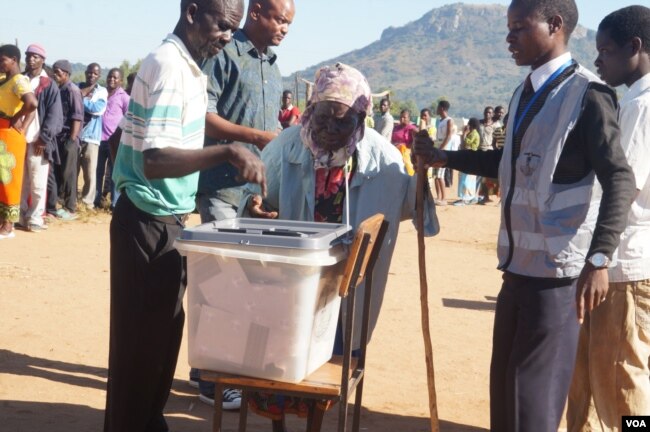 Polling monitors offer assistance as an elderly woman casts her vote in Tuesday's election in Malawi. (L Masina/VOA)