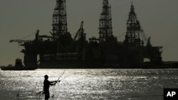 FILE - A man fishes near docked oil drilling platforms, in Port Aransas, Texas, May 8, 2020. The U.S. Interior Department on Nov. 17, 2021, is auctioning vast oil reserves in the Gulf of Mexico estimated to hold up to 1.1 billion barrels of crude.