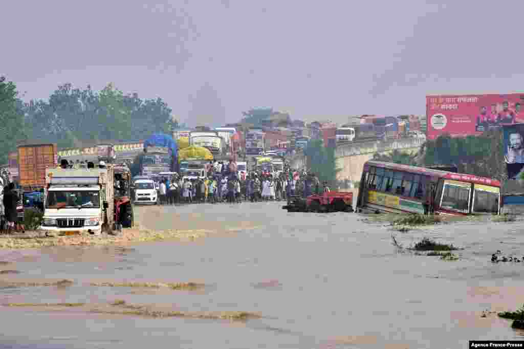 Commuters stand along a section of a flooded national highway after the Kosi River overflowed following heavy rains near Rampur in India&#39;s Uttar Pradesh state.