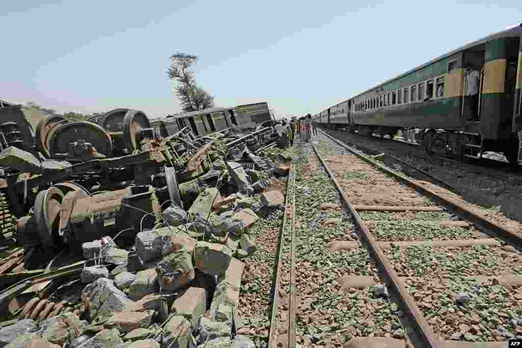 Passengers, at right, look out from a train as they travel next to the wreckage of a train after restoration of the rail track in Daharki, Pakistan, a day after a packed inter-city train ploughed into another express that had derailed, killing at least 63 people.