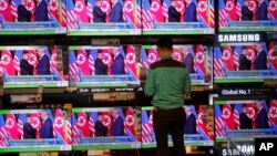 A man watches TV screens showing U.S. President Donald Trump, right, meeting with North Korean leader Kim Jong Un in Singapore, during a news program In Hong Kong, June 12, 2018.