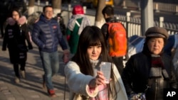 In this Feb. 28, 2016 photo, online web performer Wang Weiying, 18, broadcasts a live stream from her smartphone as she walks down a street in Beijing. Wang has turned to one live broadcast site, Huajiao, to earn money to study abroad. (AP Photo/Mark Schiefelbein)