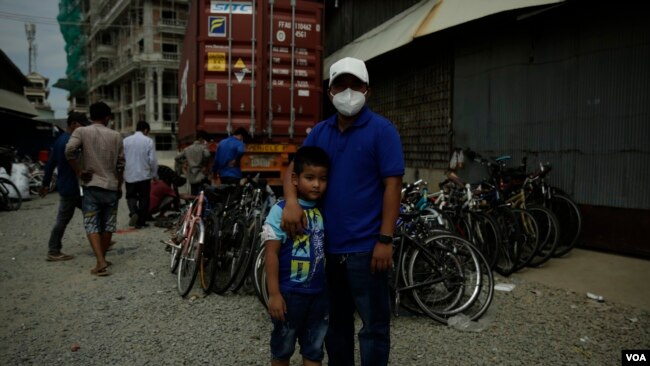 Em Savin stands outside his shipping container as his team wraps up loading and repairing bikes.(Kiana Duncan/VOA Khmer)