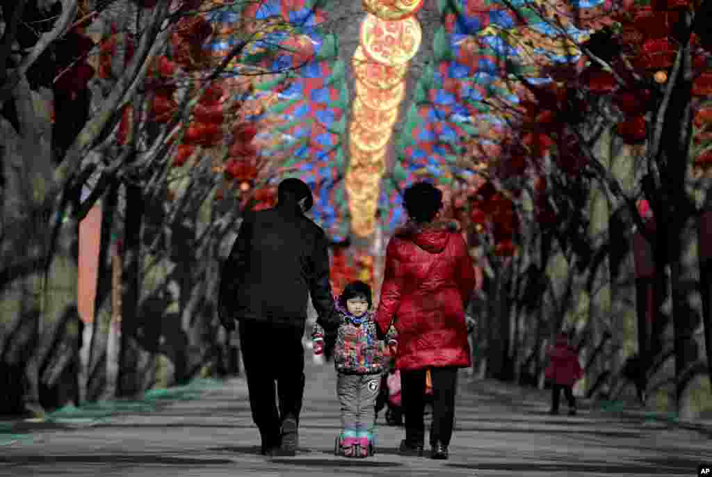 An&nbsp;elderly Chinese couple holds a child standing on a scooter as they walk under colorful decorations for a temple fair ahead of the Chinese Lunar New Year at Ditan Park in Beijing, Feb. 2, 2016. Chinese will celebrate the Lunar New Year on Feb. 8