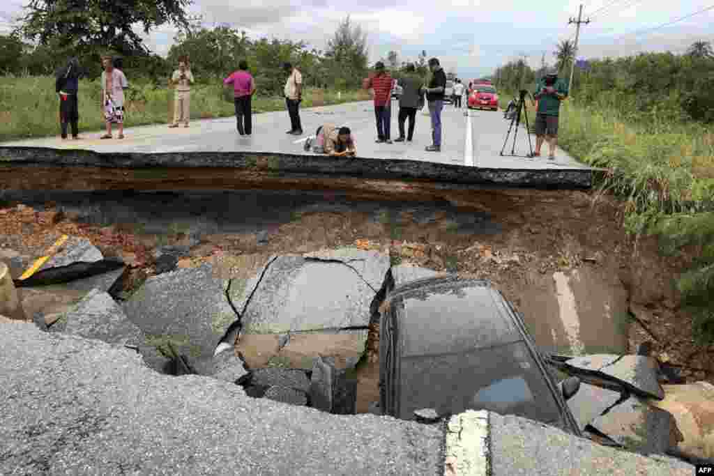 People take photos of a road that collapsed due to heavy flooding in the southern Thai district of Songkhla.