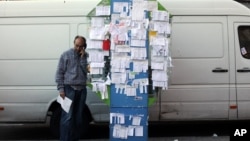 A man talks from a public phone booth covered with various personal ads including job offers, jobs wanted and rooms for rent, in Madrid, Spain, Nov. 6, 2013. 