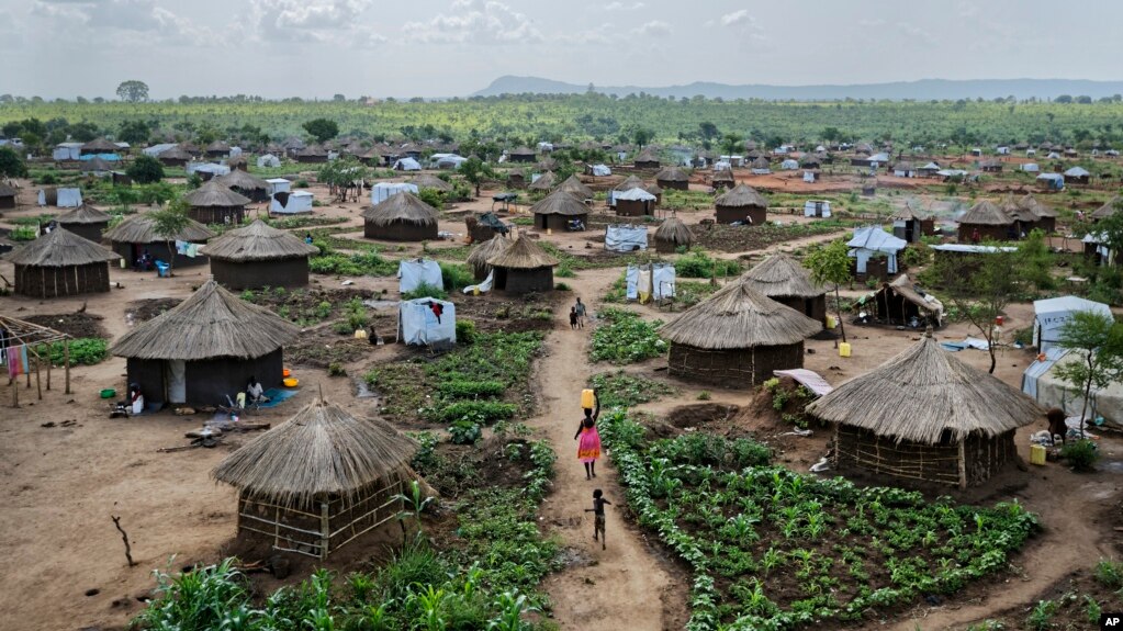 FILE - Women and children return home with plastic containers of water, in a section of the sprawling complex of mud-brick houses and tents that makes up the Bidi Bidi refugee settlement in northern Uganda, June 9, 2017.