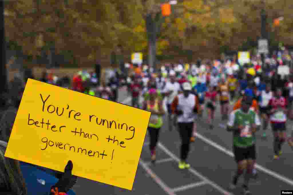 Seorang penonton membawa poster bertuliskan 'Anda berlari lebih cepat dari pemerintah' saat para pelari Maraton New York 2013 melewati wilayah Manhattan. (Reuters/Eduardo Munoz)