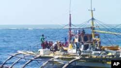 In this photo provided by Renato Etac, Chinese Coast Guard members, wearing black caps and orange life vests, approach Filipino fishermen as they confront them off Scarborough Shoal at South China Sea in northwestern Philippines, Sept. 23, 2015.