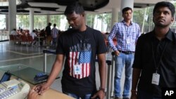 FILE - An Infosys employee sports a t-shirt featuring a U.S. flag as he buys coupons for lunch while others wait for their turn at company headquarters in Bangalore, India, April 15, 2016. 