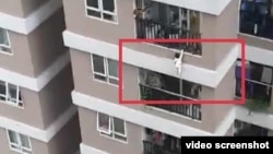 Bé gái 3 tuổi bám vào lan can tầng 12 trước khi rơi xuống mái tôn, nơi anh Nguyễn Ngọc Mạnh leo lên để chờ đỡ cháu bé.