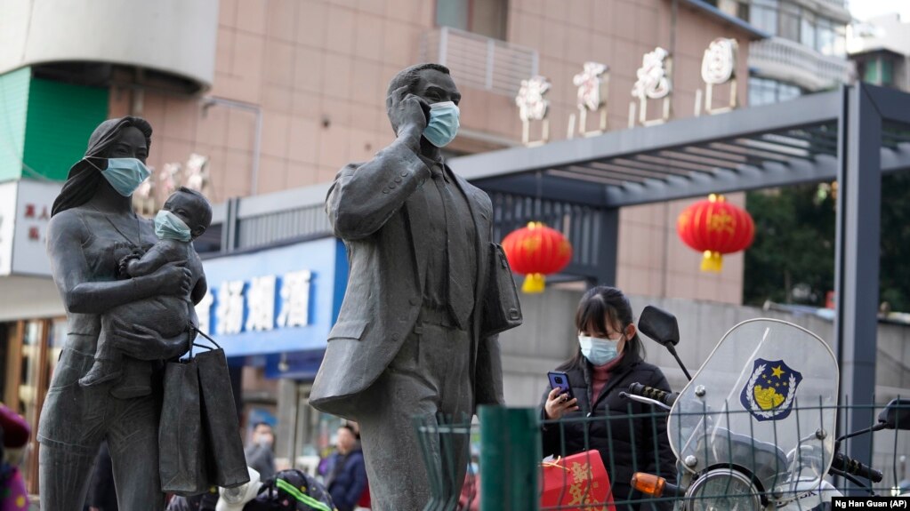 资料照片：在中国武汉市，一名女子正走过带着口罩的雕塑面前。世卫组织新冠溯源专家小组当时正在武汉考察。（2021年1月29日）(photo:VOA)