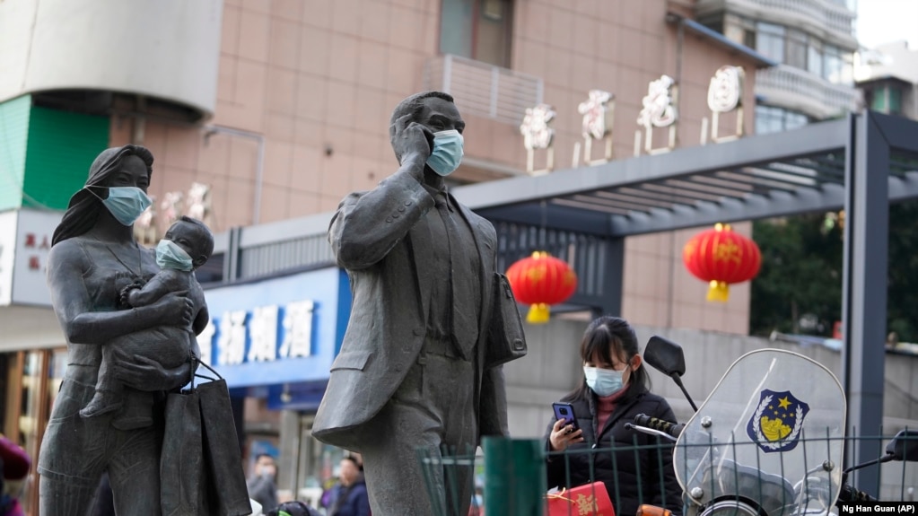 资料照片：中国武汉市，一名女子正走过带着口罩的雕塑面前。期间，世卫组织新冠溯源专家小组正在武汉考察。（2021年1月29日）(photo:VOA)