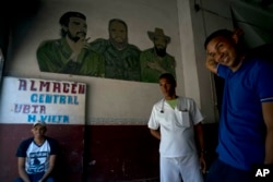 Men take a break inside a warehouse featuring a mural of revolutionary leaders Camilo Cienfuegos, right, Ernesto "Che" Guevara, left, and Fidel Castro, in Havana, Cuba, April 17, 2019.
