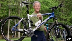 FILE - President George W. Bush lifts his bicycle before taking a mountain bike ride in Beltsville, Md. 