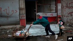 Un hombre y un niño llevan provisiones de alimentos distribuidas por las fuerzas de seguridad iraquíes cerca de la línea de frente durante la lucha contra el Estado islámico en el oeste de Mosul, Irak, miércoles, 15 de marzo de 2017.