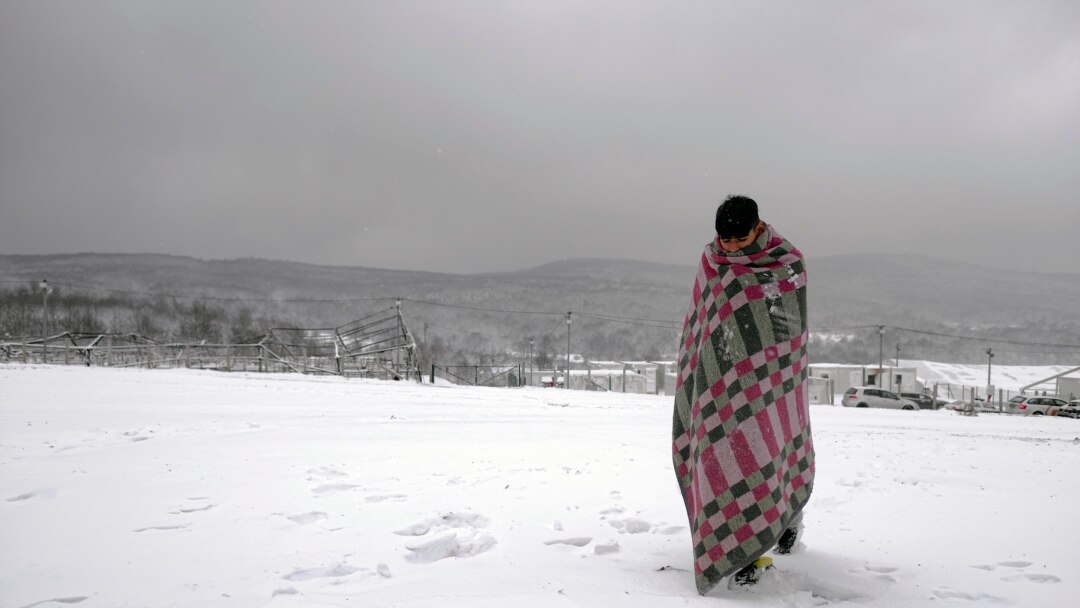 A migrant walks through the snow wrapped in a blanket at the Lipa camp northwestern Bosnia, near the border with Croatia, Saturday, Dec. 26, 2020.