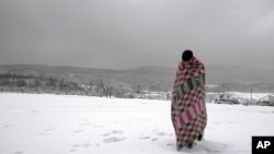 Un migrant traverse la neige enveloppé dans une couverture au camp de Lipa au nord-ouest de la Bosnie, près de la frontière avec la Croatie, le samedi 26 décembre 2020.