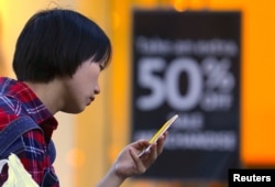 FILE - A shopper looks at her phone in front of a sales sign displayed in a window of a retail store at a shopping center in central Sydney, Australia.