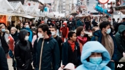 FILE - People wear face masks to curb the spread of the coronavirus as they walk in the alley of a funfair in Paris, France, Dec. 29, 2021.