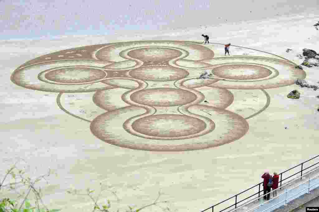 Sand artist Marc Treanor creates a work on the North Beach at Tenby Harbour, Pembrokeshire, Wales, Britain.