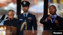 India's President Pranab Mukherjee speaks at the podium as the unidentified sign language nterpreter (R) punches the air beside him during a memorial service for late South African President Nelson Mandela at the FNB soccer stadium in Johannesburg, Dec. 10, 2013.