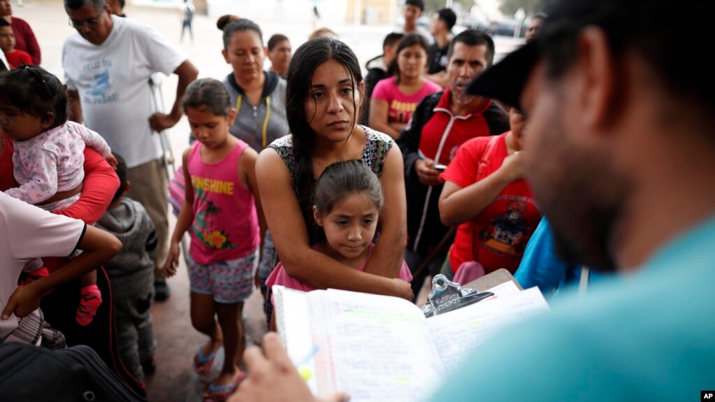 Una mujer del estado mexicano de MichoacÃ¡n que no dio su nombre y su hija, escuchan la lectura de una lista de personas que cruzarÃ¡n a EE.UU. para comenzar el proceso de solicitud de asilo el jueves 26 de julio de 2018, cerca de el puerto de entrada a San Ysidro en Tijuana, MÃ©xico. (AP Photo / Gregory Bull).