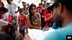 A woman from the Mexican state of Michoacan who did not give her name stands with her daughter as names are read off a list of people who will cross into the United States to begin the process of applying for asylum Thursday, July 26, 2018, near the San Ysidro port of entry in Tijuana, Mexico. 