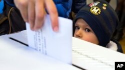 A child looks at a ballot being cast at a polling station in Zagreb, Croatia, Nov. 8, 2015. 