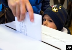 A child looks at a ballot being cast at a polling station in Zagreb, Croatia, Nov. 8, 2015.