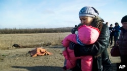 FILE - A woman with her child and others pass body of a man, who died in a land mine explosion near a frontline crossing to Ukrainian government-controlled territory, in the war conflict-hit Donetsk region, near Donetsk, eastern Ukraine, Feb. 10, 2015. The U.N. children’s fund calls on Feb. 21, 2016, the daily suffering endured by more than one-half million Ukrainian children victimized by two years of conflict intolerable. 
