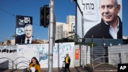 Warga Israel melewati baliho pemilu dengan gambar pemimpin partai Likud PM Benjamin Netanyahu (kanan) dan partai oposisi pimpinan Benny Gantz (kiri) menjelang pemilu ketiga (1/3). 