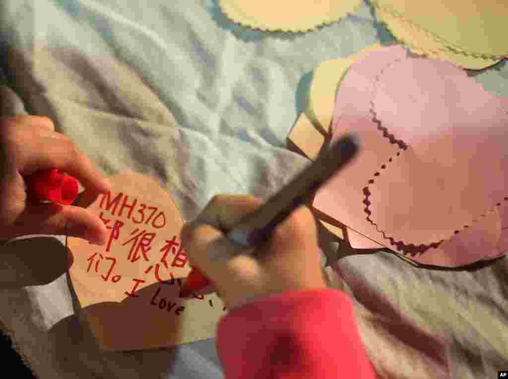 A girl writes a note which she will hang on a memorial for the people on Flight MH370 in Kuala Lumpur, March 30, 2014.