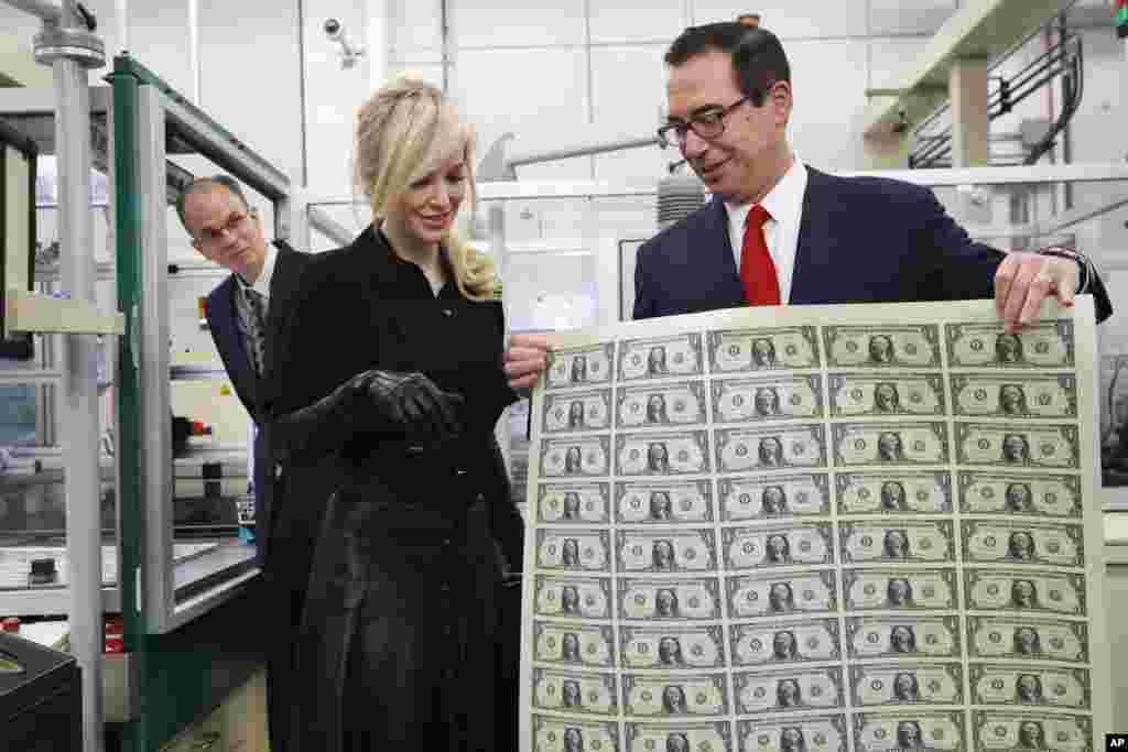 Treasury Secretary Steven Mnuchin shows his wife Louise Linton a sheet of new $1 bills, the first currency notes bearing his and U.S. Treasurer Jovita Carranza&#39;s signatures, at the Bureau of Engraving and Printing (BEP) in Washington, D.C., No. 15, 2017.